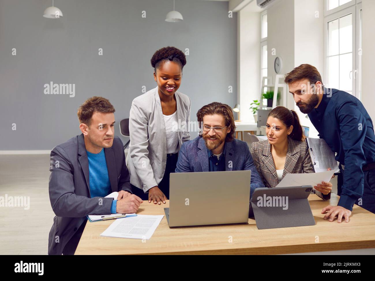 Diverse team of happy people use a laptop and tablet while working on a business project together Stock Photo