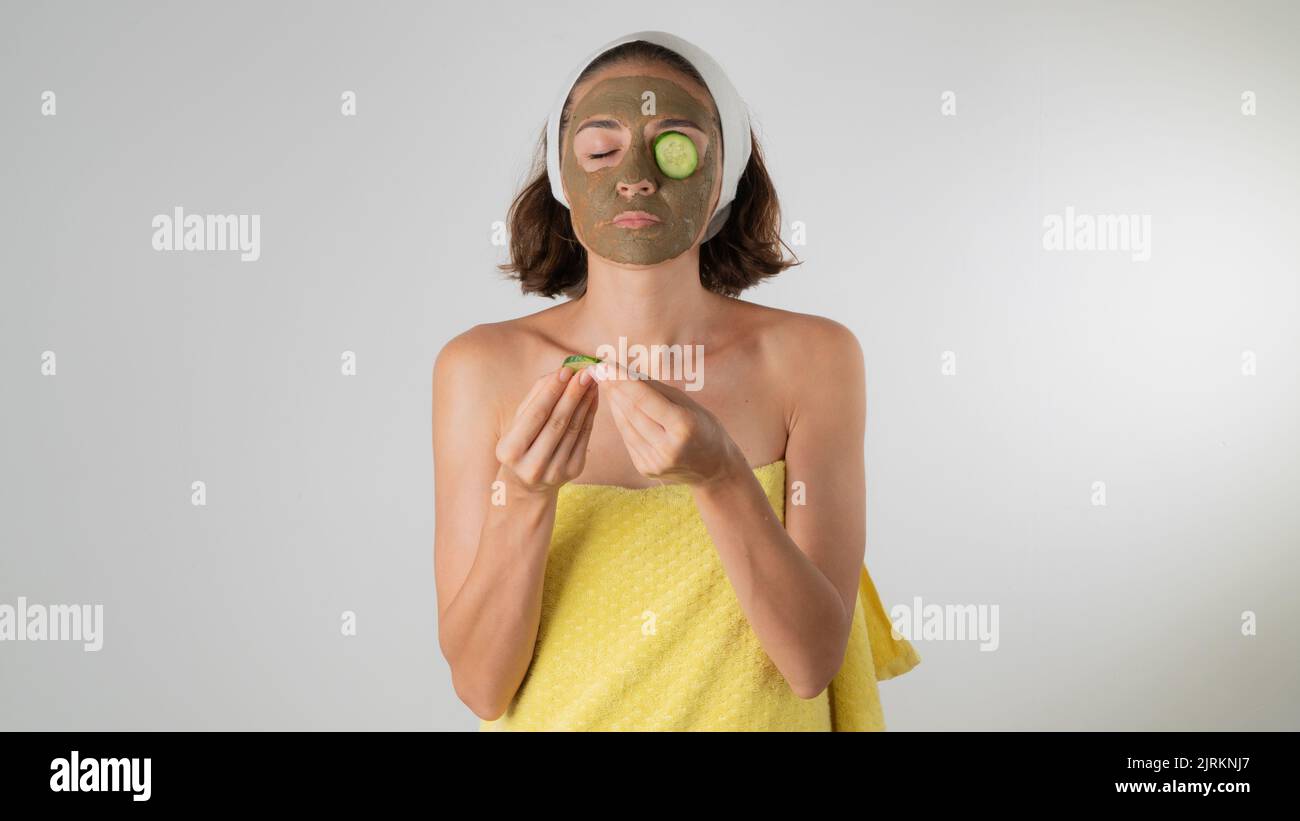 A woman in a clay mask puts a circle of cucumber on the eye - facial skin care at home. High quality photo Stock Photo
