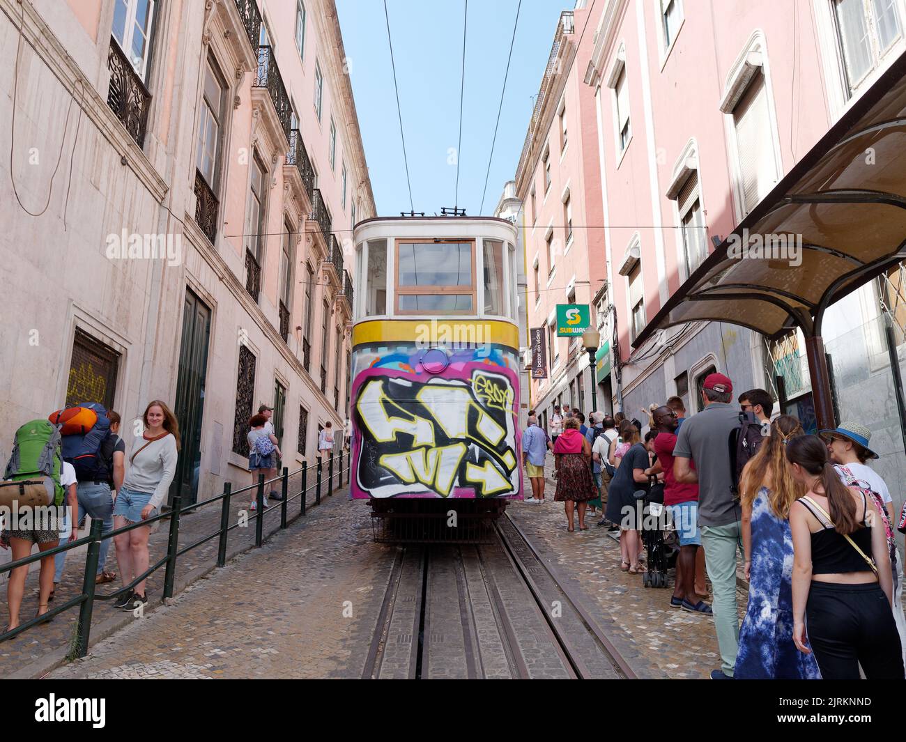 Tram aka Streetcar aka Trolley in Lisbon. People gather by the stop and tourists with back packs walk past. Portugal Stock Photo