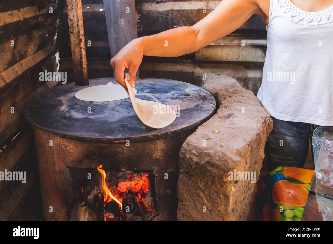 A Hispanic woman cooking corn dough on a stove, making homemade