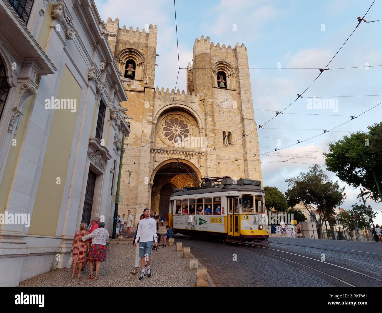 Cathedral of Saint Mary Major aka Lisbon Cathedral aka Sé de Lisboa. A tram passes by in front of the Cathedral as tourists walk in the street. Stock Photo