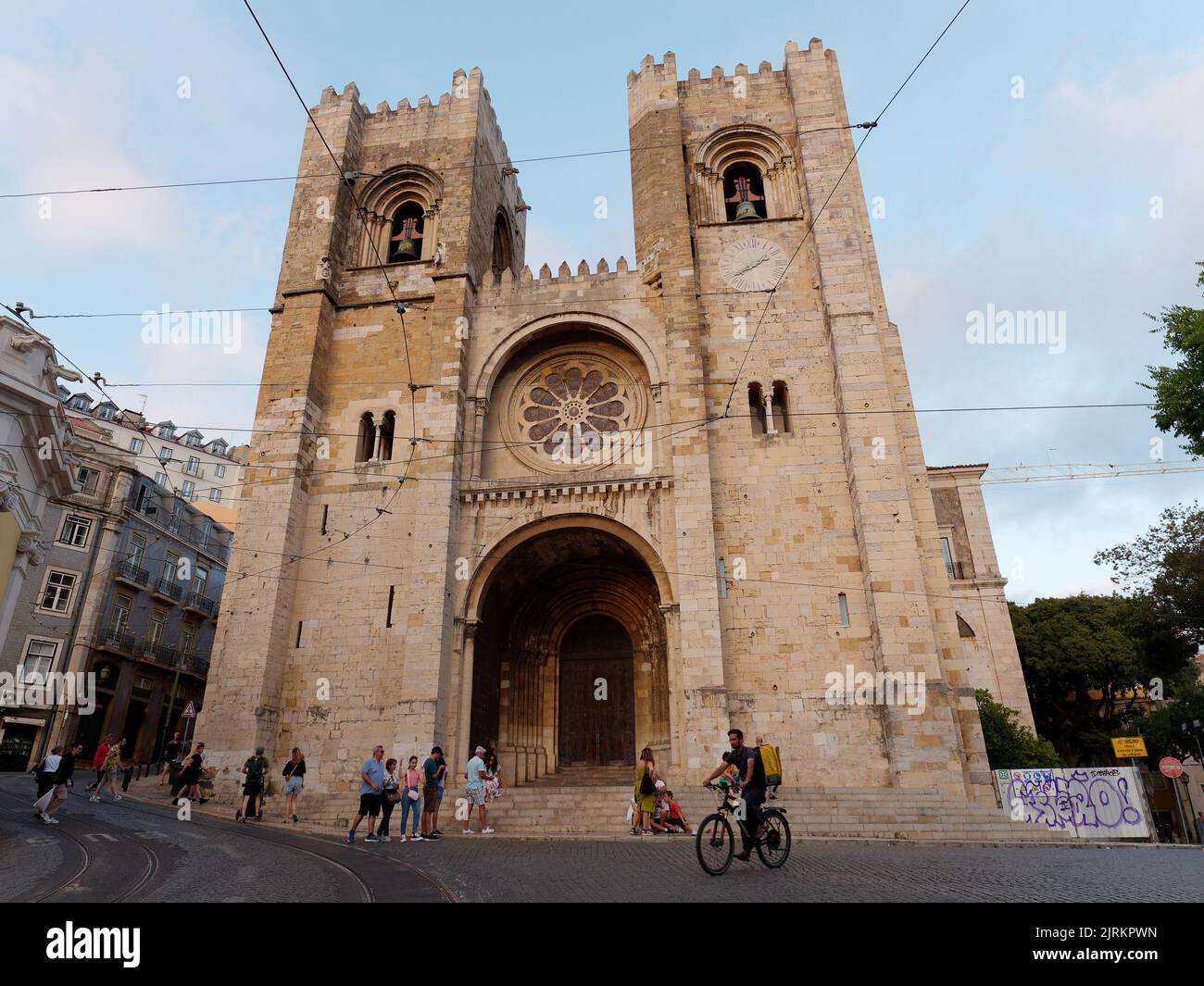 Cathedral of Saint Mary Major aka Lisbon Cathedral aka Sé de Lisboa. Tourists walk in the street and someone rides a bicycle. Stock Photo