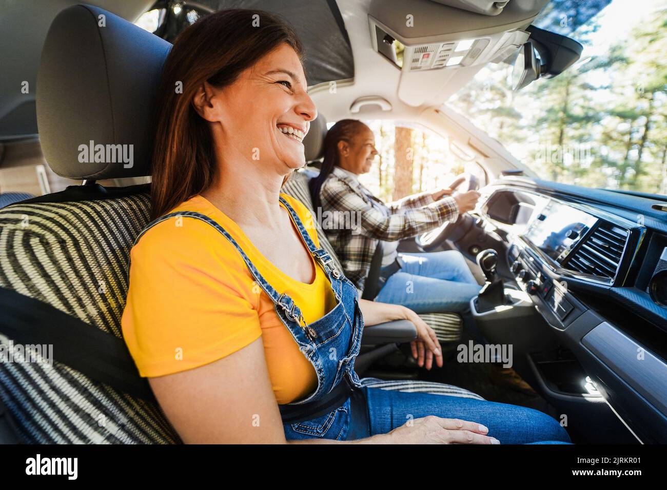 Multiracial senior friends having fun on the road with mini van camper - Focus on left woman face Stock Photo