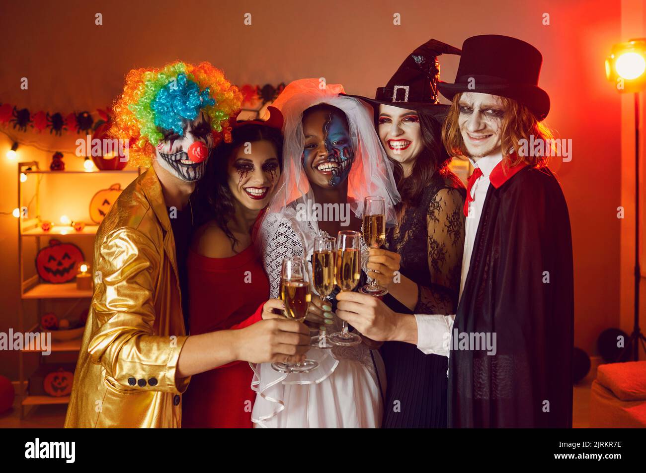 Portrait of cheerful happy adult friends with glasses of champagne at home party for Halloween. Stock Photo