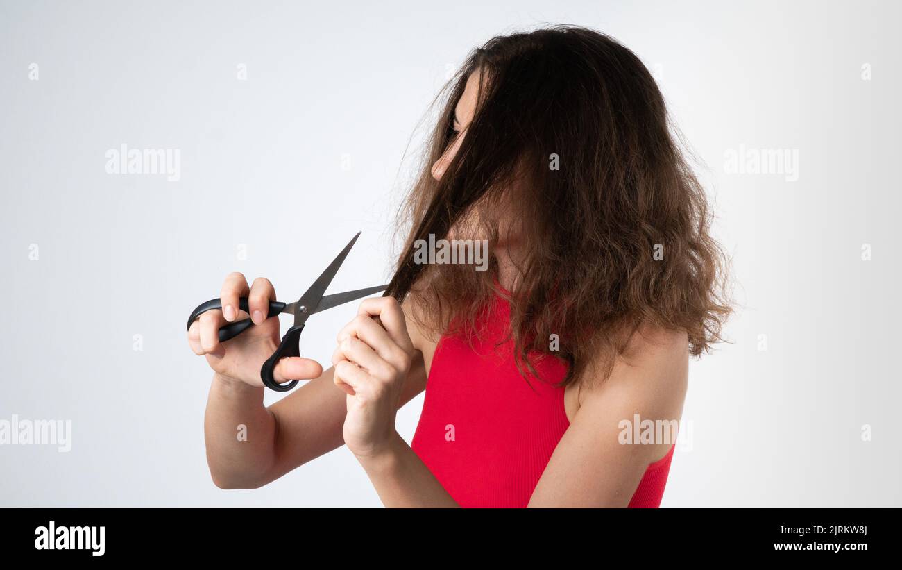 A woman with scissors cuts off the split ends of naughty, unhealthy