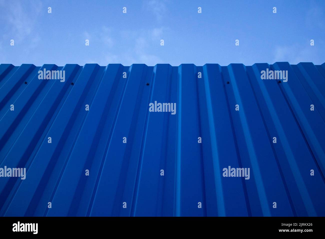 Texture of a metal blue painted old dark fence wall with a sky in the background. Stock Photo