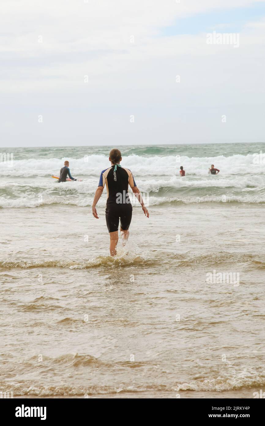 Woman in wetsuit running out to sea from behind, North
