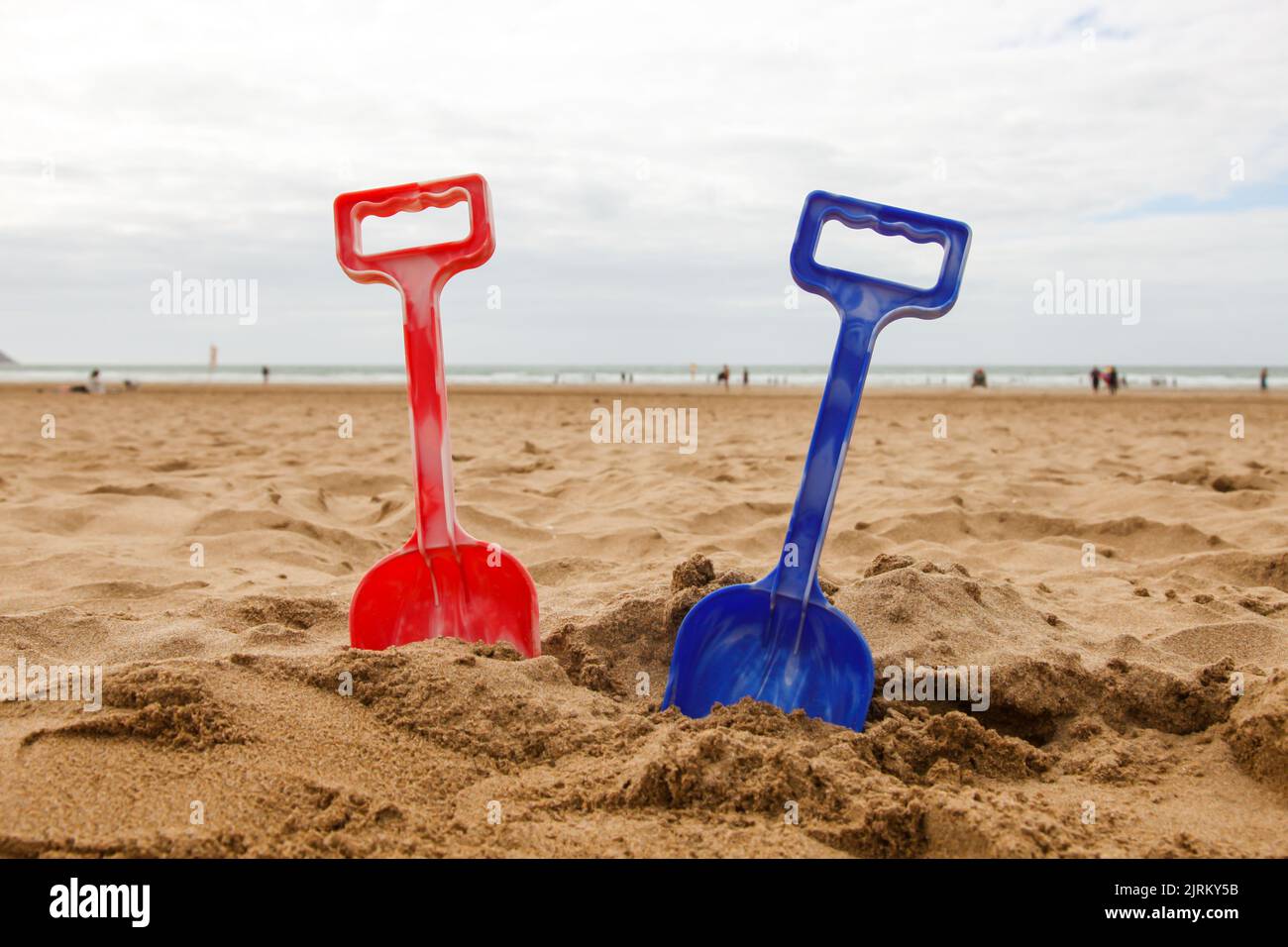 Gender specific pink and blue child toy plastic spades in sand, Woolacombe, North Devon, England, UK Stock Photo