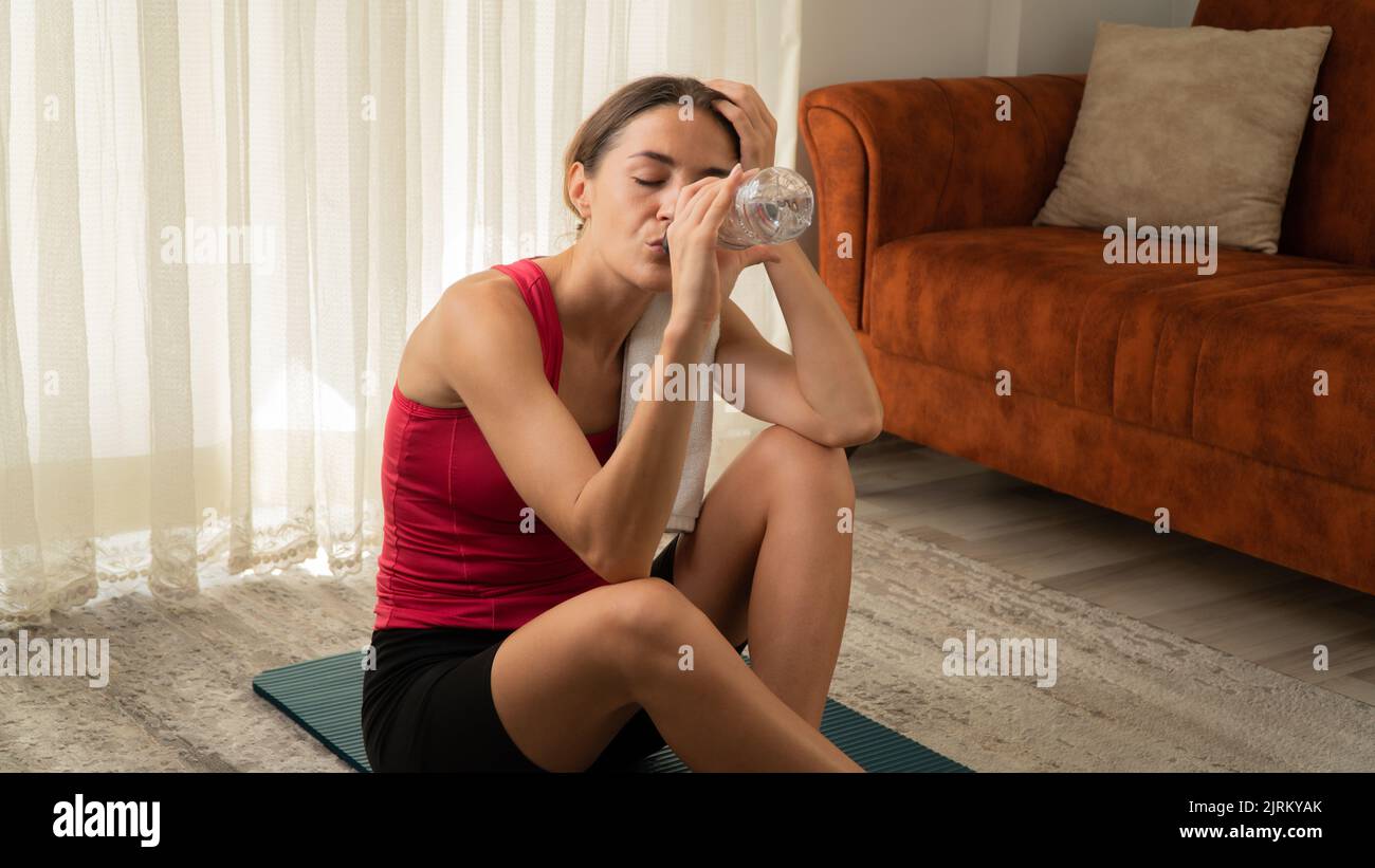 A tired woman after a workout drinks water on the mat of the house. High quality photo Stock Photo