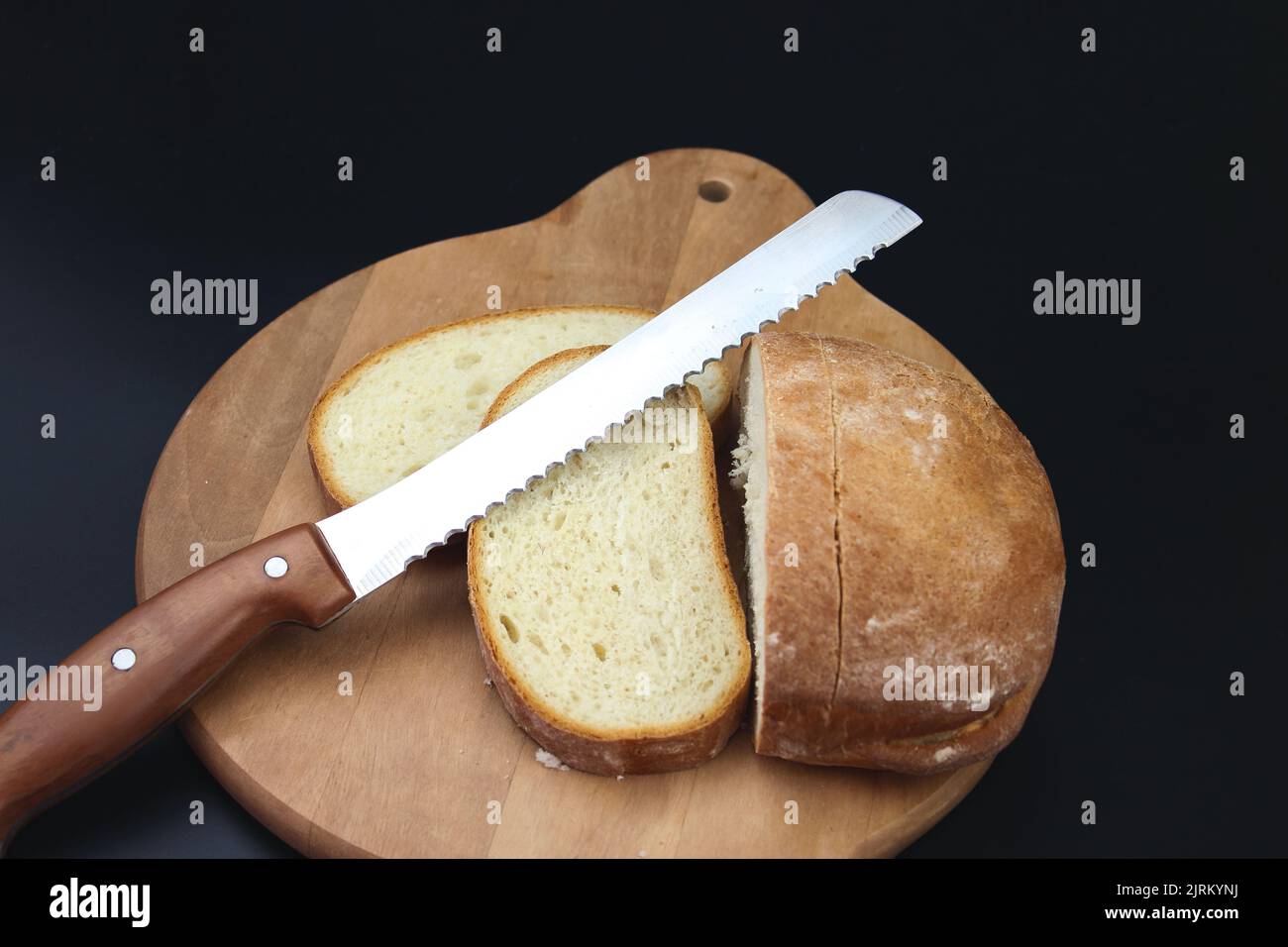 Freshly baked Bread, sliced with a serrated bread knife on a wooden cutting board. Stock Photo