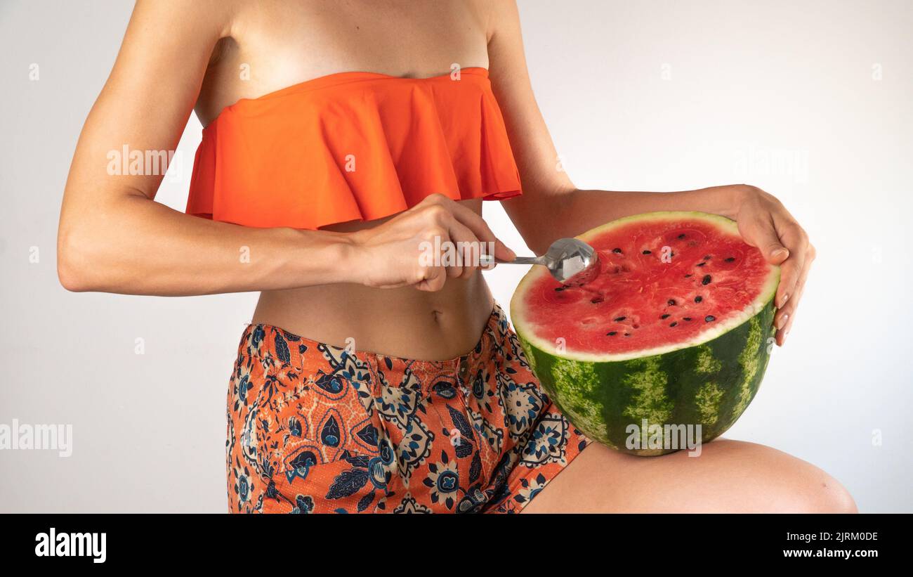 A woman in a swimsuit eats watermelon with a spoon on a white background - summer pace. High quality photo Stock Photo
