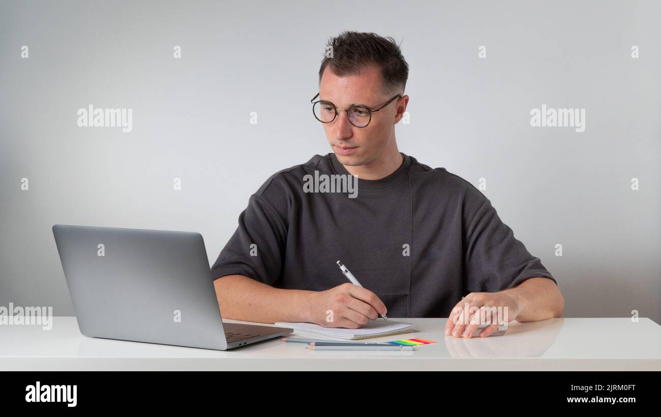A guy at a laptop makes notes in a notebook at the workplace - work and study. High quality photo Stock Photo