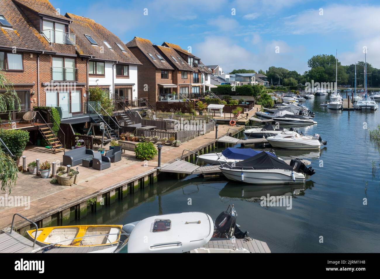 Boats on the River Stour in Christchurch, Dorset, England, UK, and exclusive properties, on a sunny summer day Stock Photo