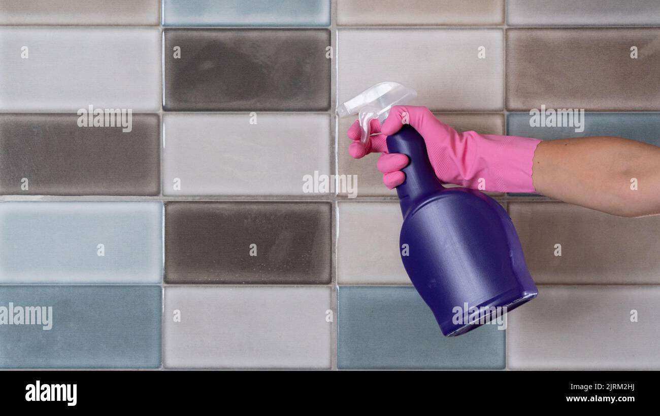 A woman in rubber gloves washes tiles in the kitchen or bathroom with a