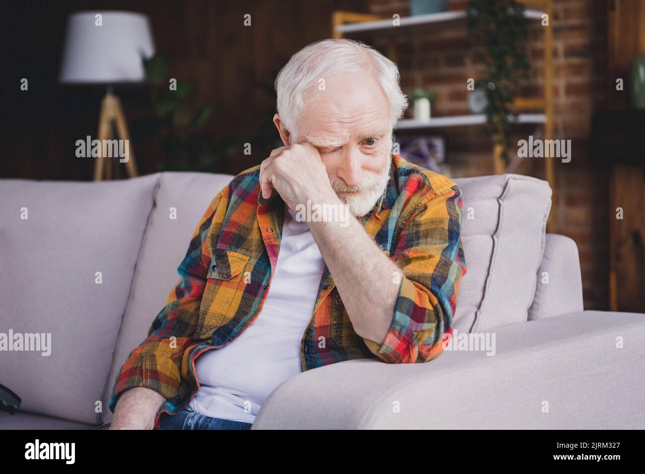 Photo of sad depressed man pensioner wear checkered shirt crying sitting sofa indoors house room Stock Photo