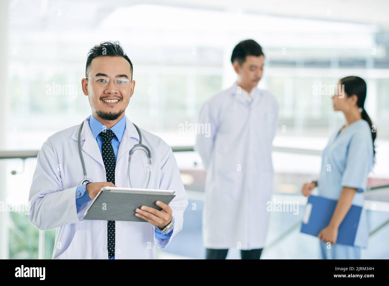 Cheerful mature Vietnamese doctor working on tablet computer Stock Photo