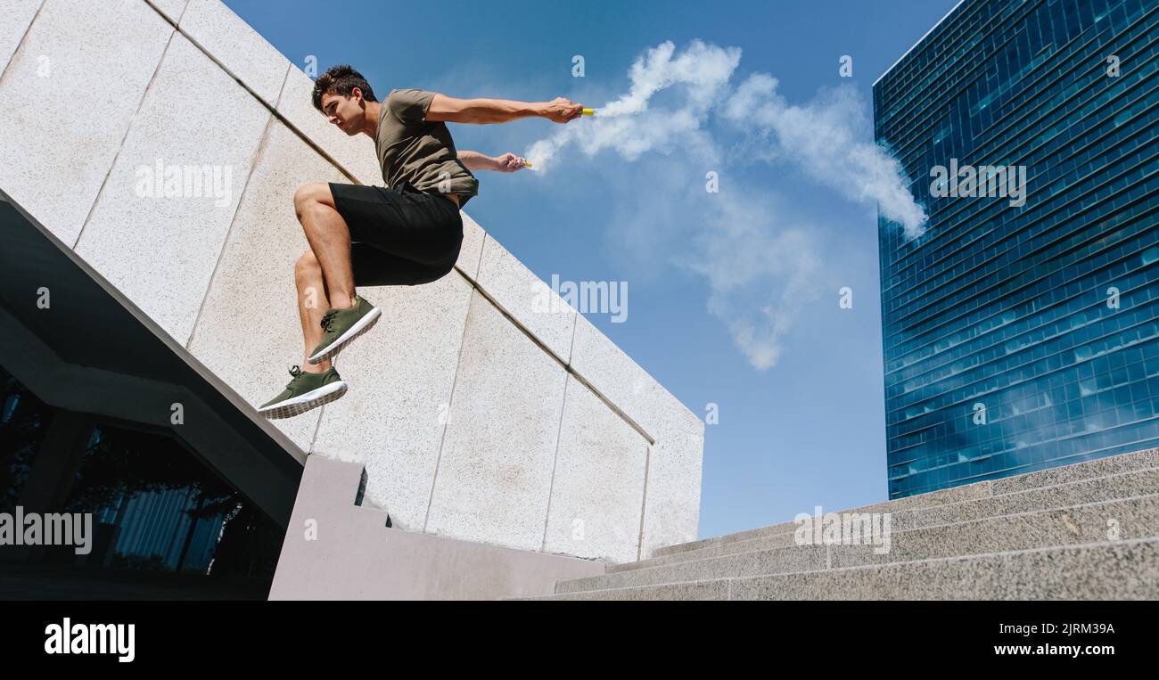Free runner jumping over an obstacle with smoke grenades. Young sportsman doing parkour stunts outdoors in the city. Stock Photo