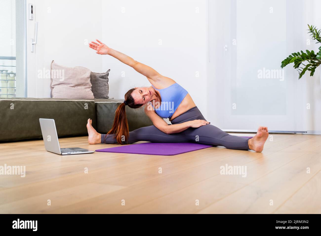 Beautiful and athletic fit girl doing stratching at home at loft studio, using laptop Stock Photo