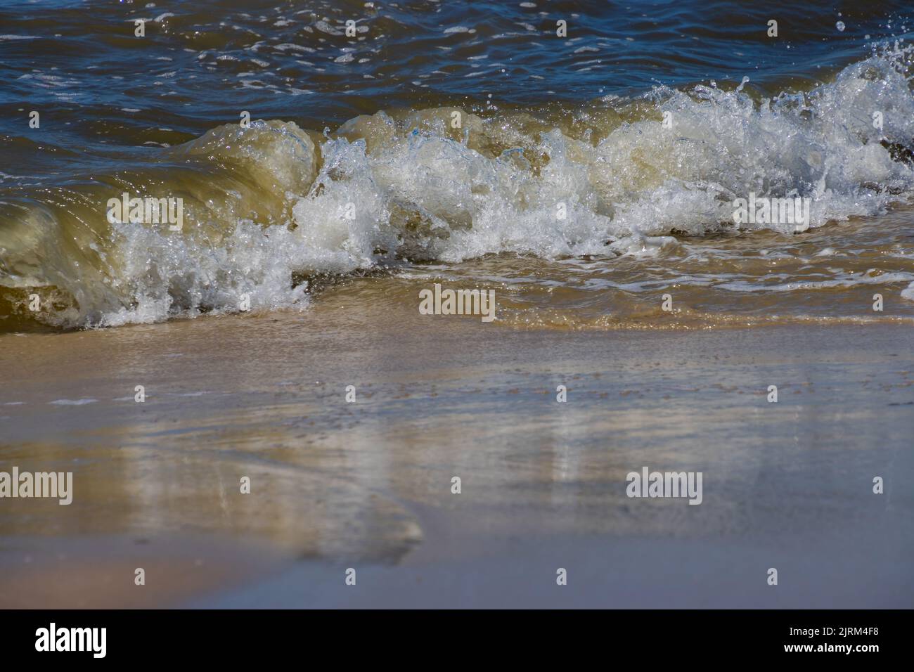 Breaking waves at a sandy beach on a sunny day Stock Photo