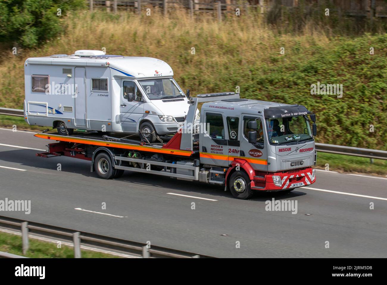 John Macadam & Son Rescue Ltd, 24 Hour Roadside Assistance & Car Rescue. 2020 Volvo FL816 4x2 Crew cab flatbed lorry, 24hr roadside emergency rescue. Recovery vehicle carrying broken down caravan; travelling on the M6 motorway, UK Stock Photo