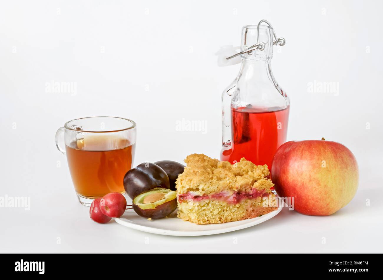 plum cake, fruit juice in a glass and in a bottle, plums and apple on a white background Stock Photo