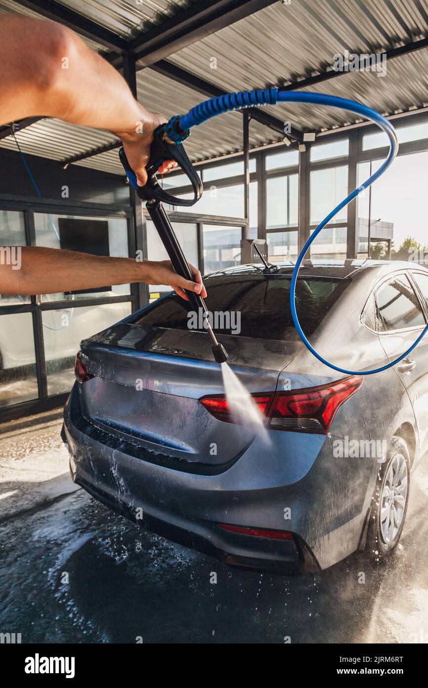 A man washes his car at a selfservice car wash using a hose with