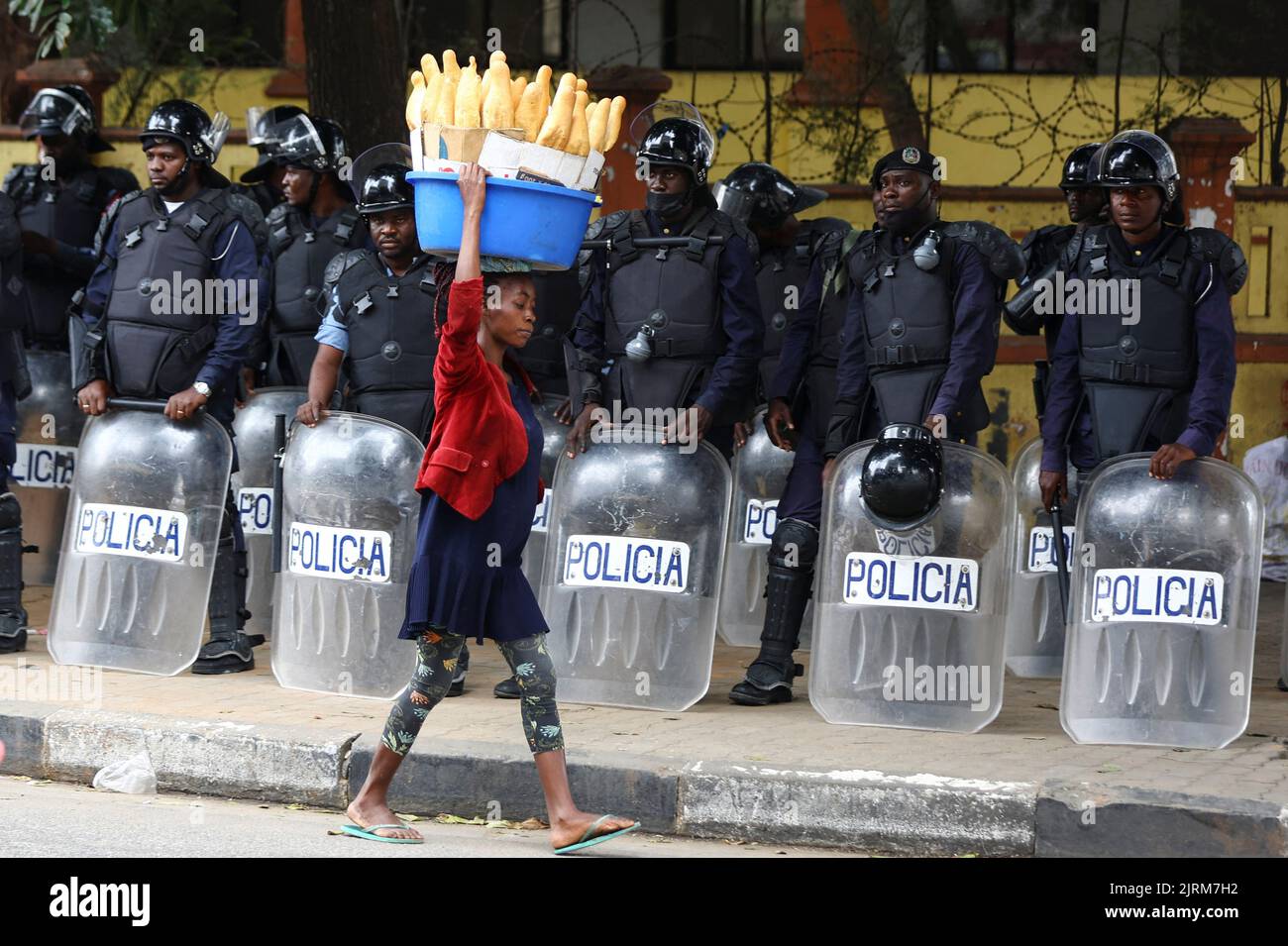 A woman walks past police officers as Angola's election commission says ruling MPLA party leads with 52% majority, after the general election close in Luanda, Angola August 25, 2022. REUTERS/Siphiwe Sibeko     TPX IMAGES OF THE DAY Stock Photo