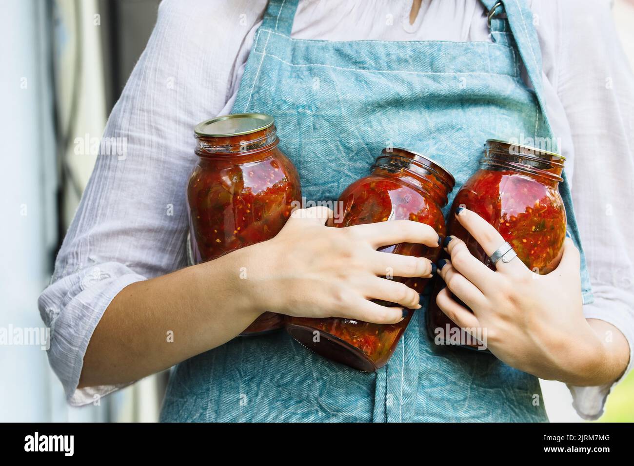 Woman's hands holding homemade canned quart mason jars of tomato salsa. Selective focus with blurred background. Stock Photo