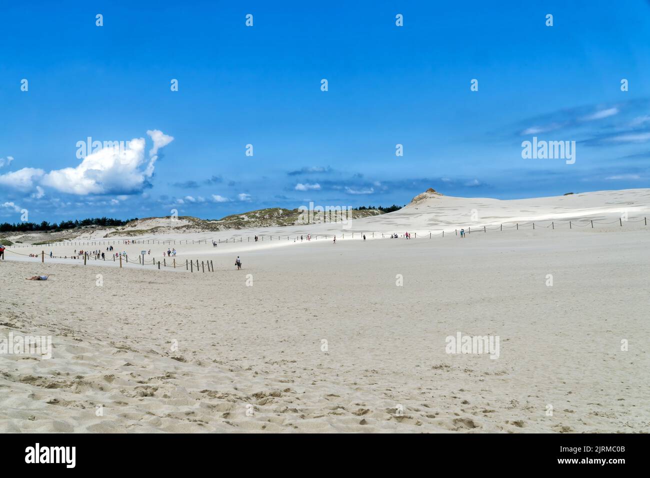 People explore in Lacka dune in Slowinski National Park in Poland. Traveling dune in sunny summer day. Sandy beach and and blue sky with white clouds. Stock Photo