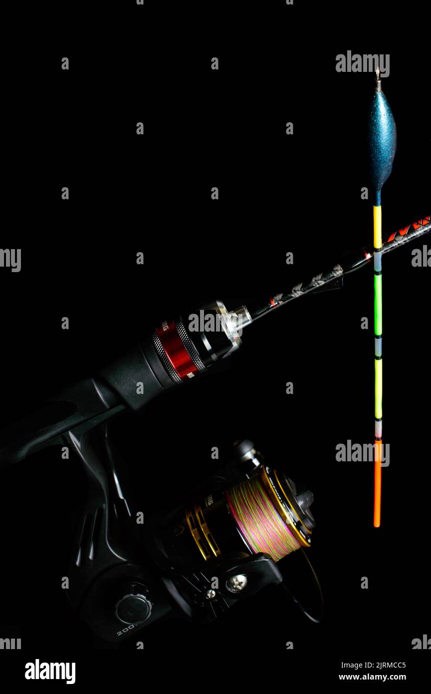 Fishing rod with a reel and colorful Fishing float on a black background. Stock Photo