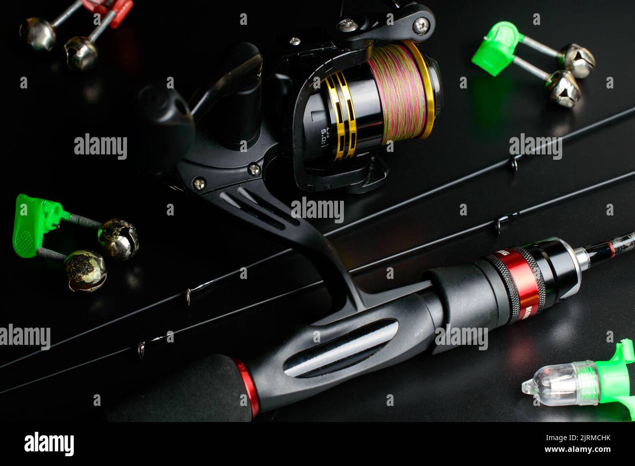 Fishing rod with reel and extra tips on a black background with small green bells. Stock Photo