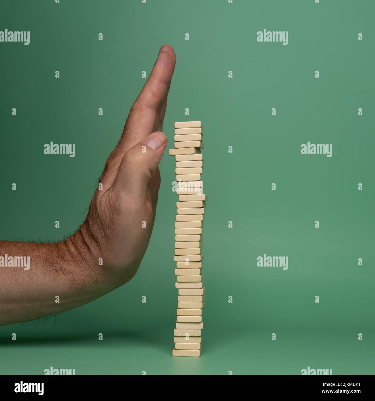 One hand protects a pile of wooden dowels from falling. The concept of protection of unstable systems Stock Photo