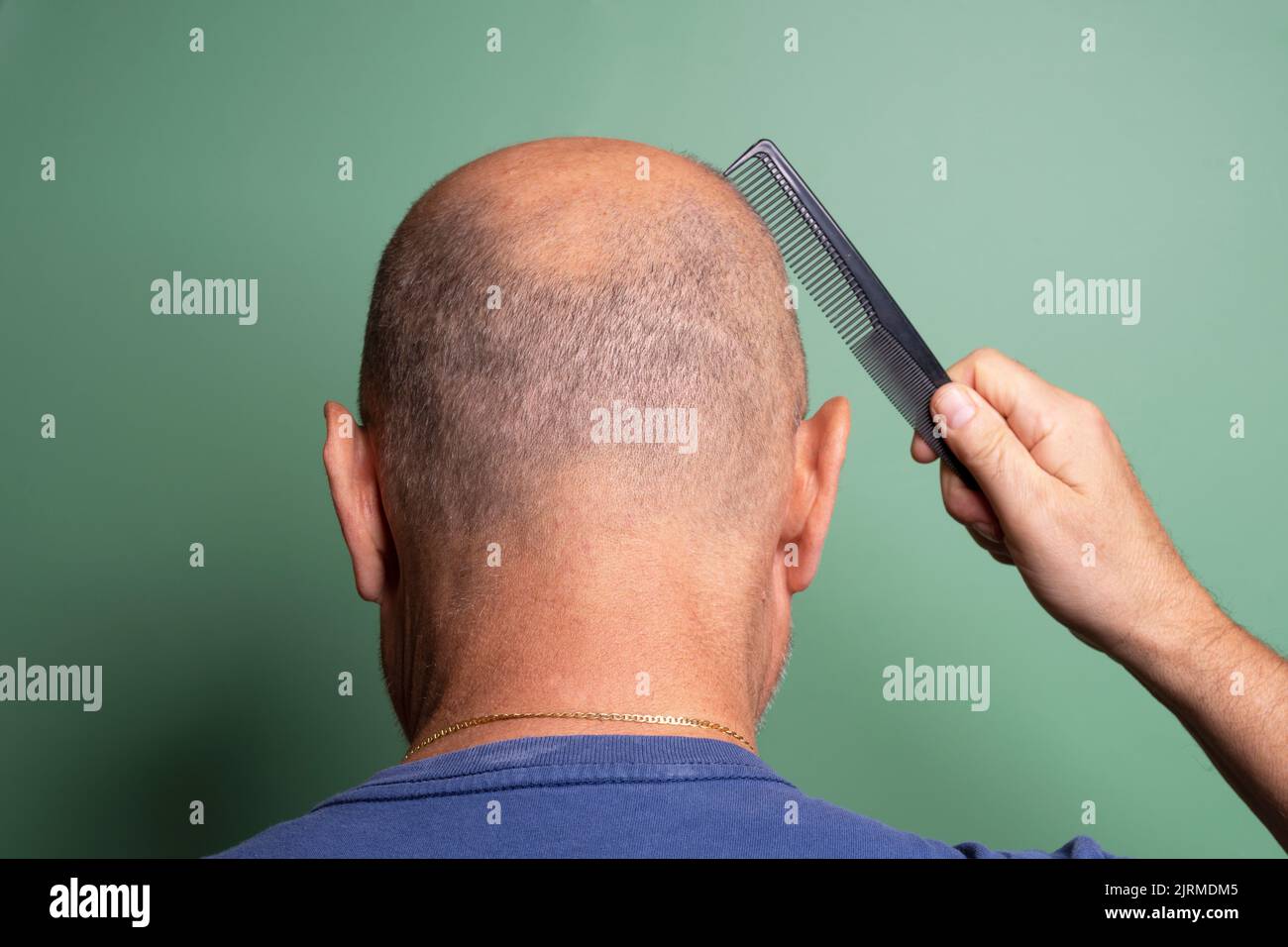 view from behind of a bald man while he combs his hair Stock Photo
