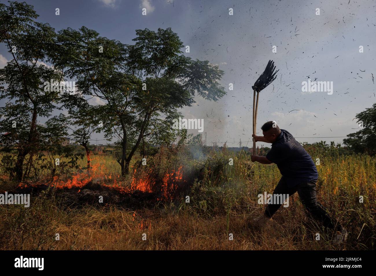 A villager attempts to put out a brush fire with a mop during a drought in Xinyao village, Nanchang city, Jiangxi province, China, August 25, 2022.  REUTERS/Thomas Peter Stock Photo
