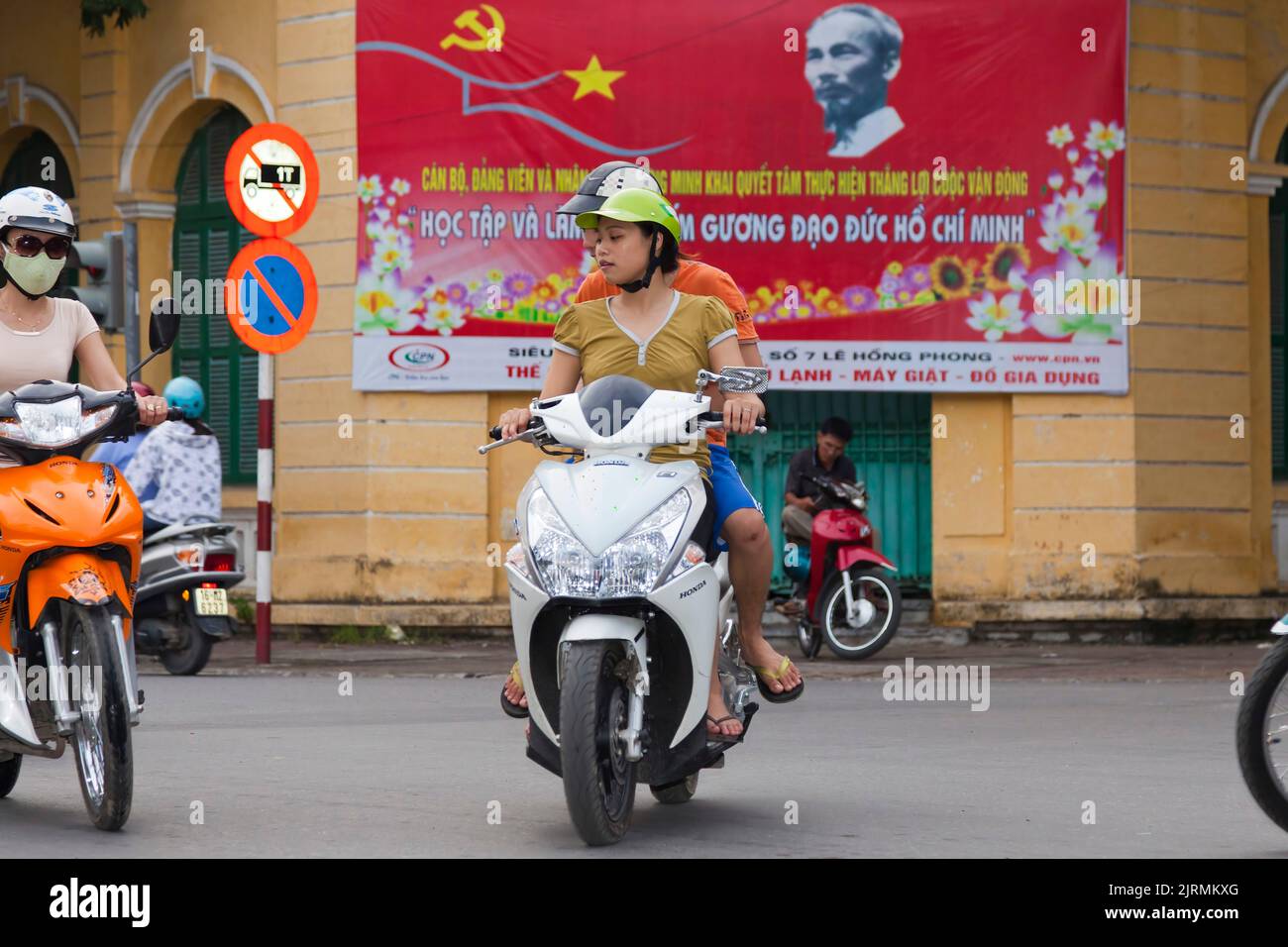 Vietnamese girls on motorcycles in front of Ho Chi Minh propaganda poster, Hai Phong, Vietnam Stock Photo