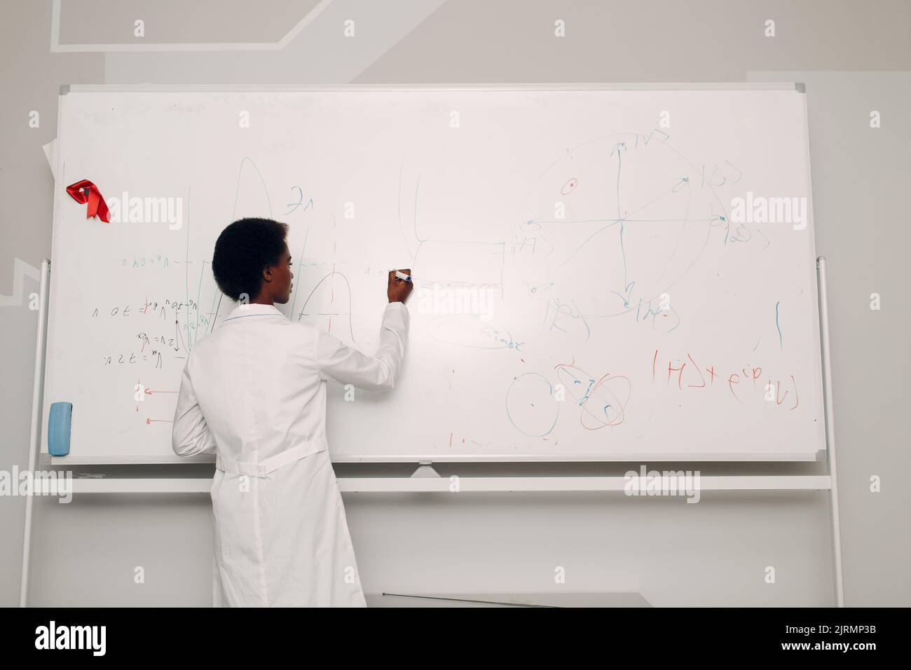 African American woman math teacher writing on blackboard with marker. Stock Photo