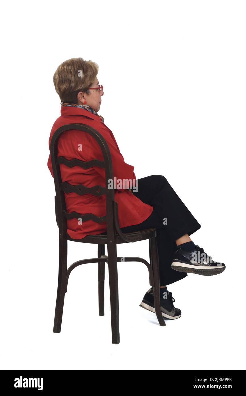 side back view of a full portrait of senior woman with shirt and pants sitting on chair  on white background Stock Photo
