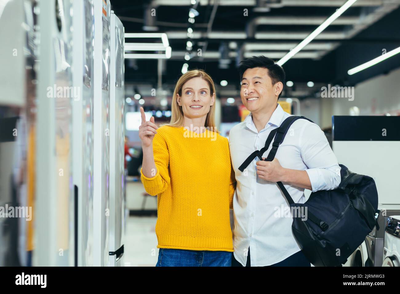 happy asian couple family man and woman make a choice choose of new household home appliances in supermarket survey Refrigerator Fridge cooler, freezer, cold store purchase and shopping Stock Photo
