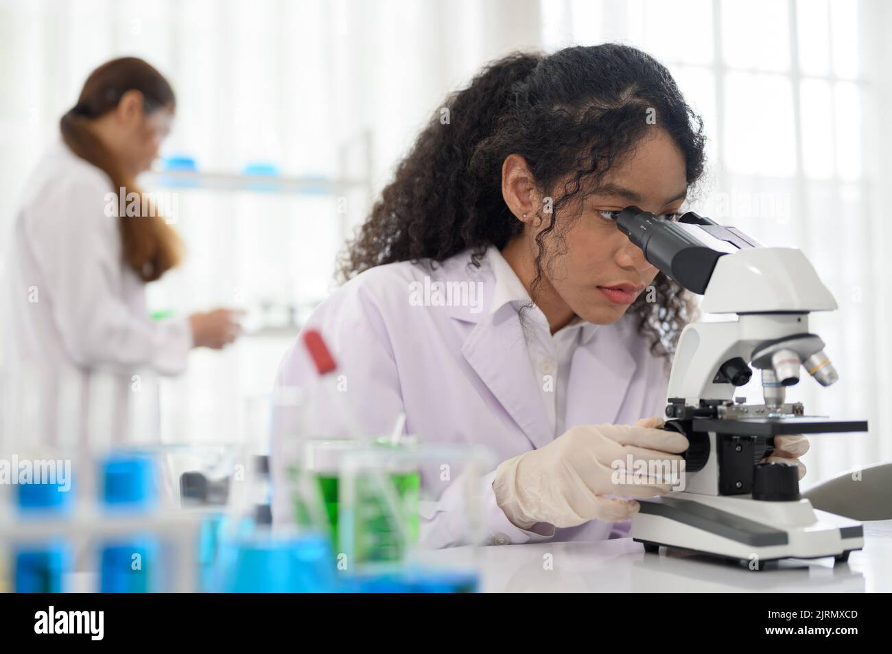 Young scientist looking in microscope while working on medical research in science laboratory Stock Photo