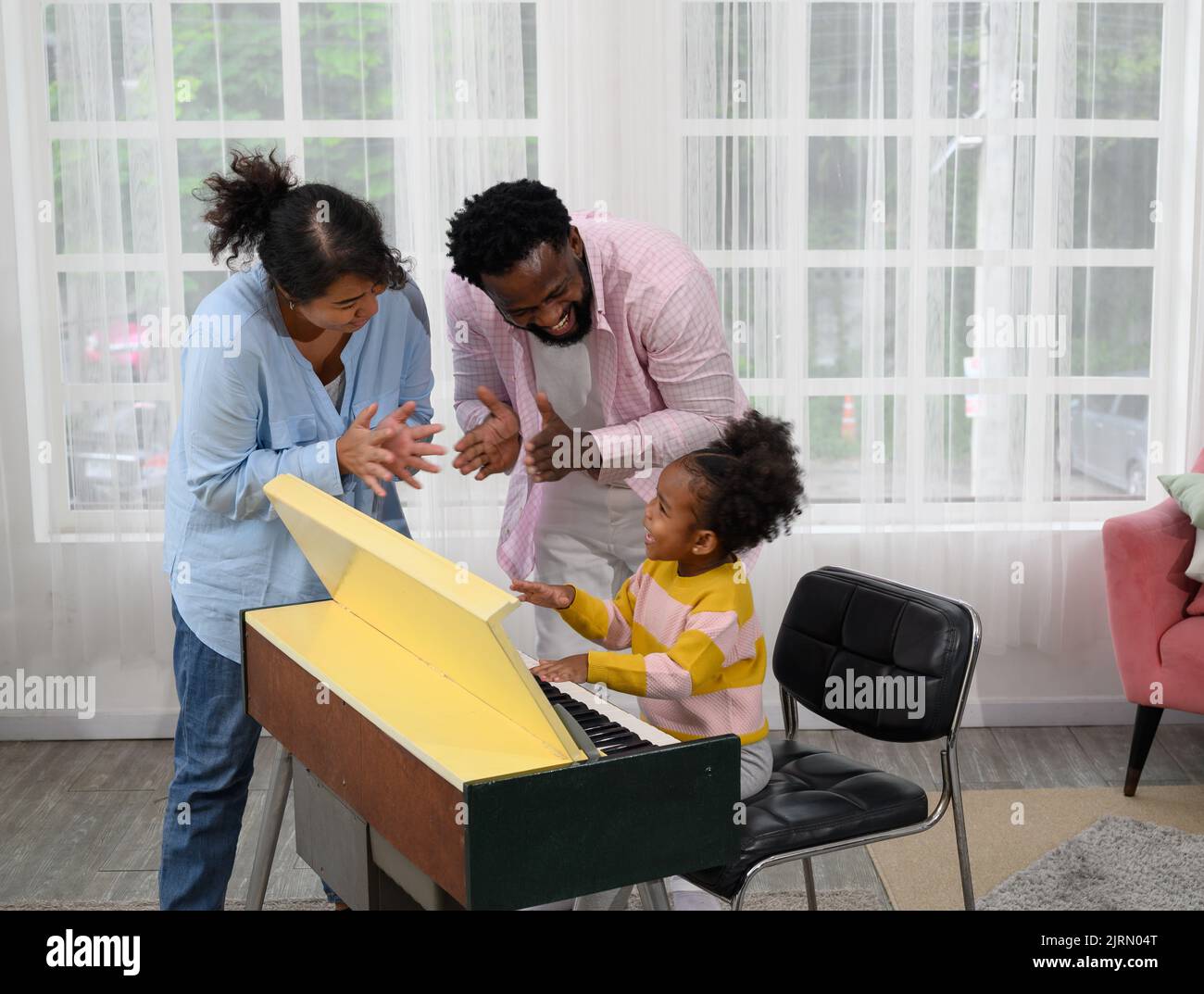 Little girl play on a piano with parent in the living room Stock Photo