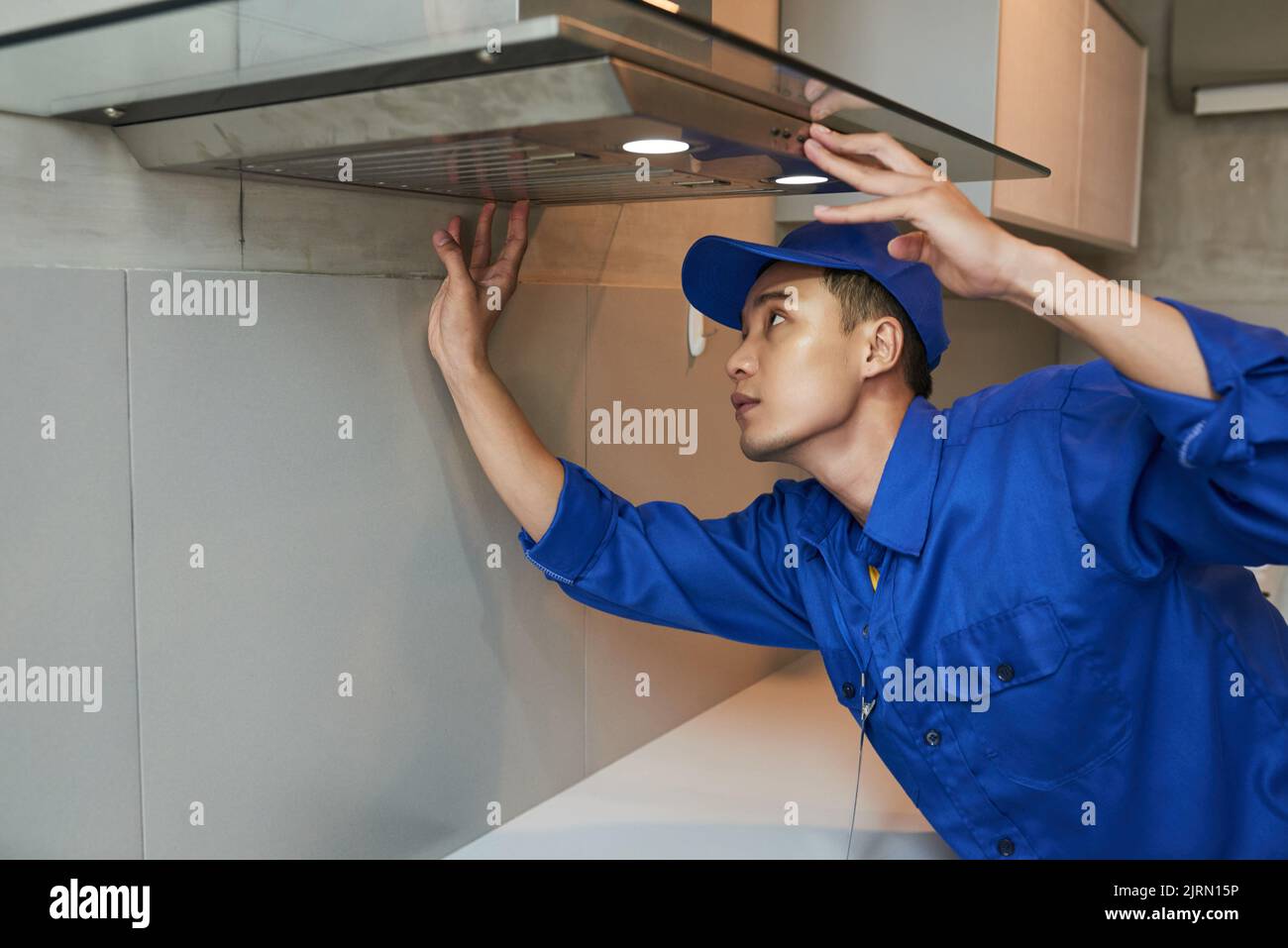 Young Vietnamese technician installing extractor hood in kitchen Stock Photo
