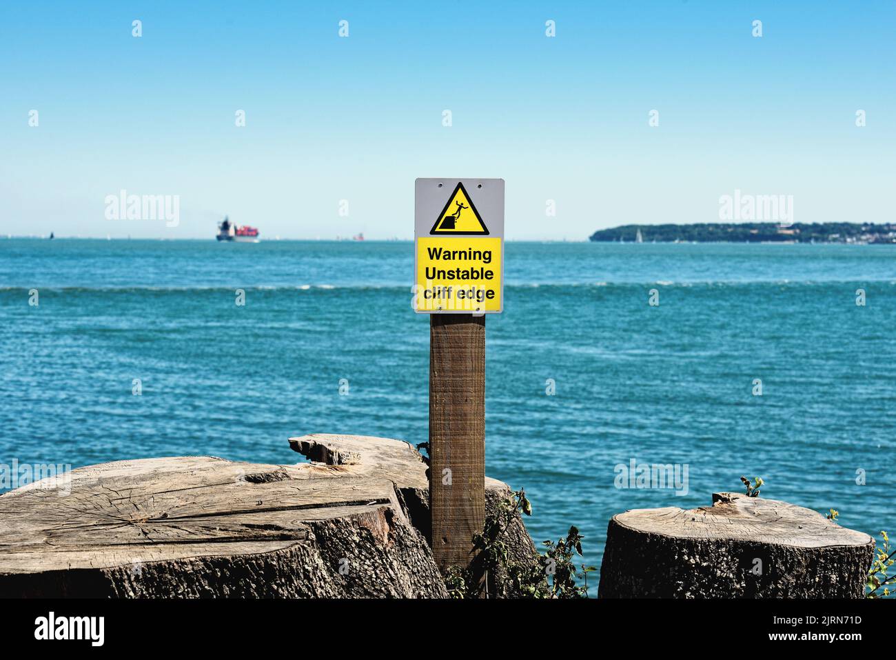 A yellow warning sign alerting the public to the dangers of an unstable cliff edge at Lepe country park with the Solent in the background Hampshire UK Stock Photo