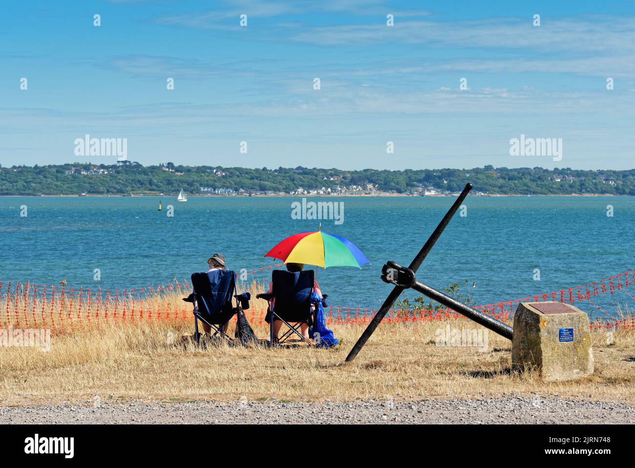 Rear view of an elderly couple sitting on chairs enjoying the view across the Solent on a summers day at Lepe country park, Hampshire England UK Stock Photo