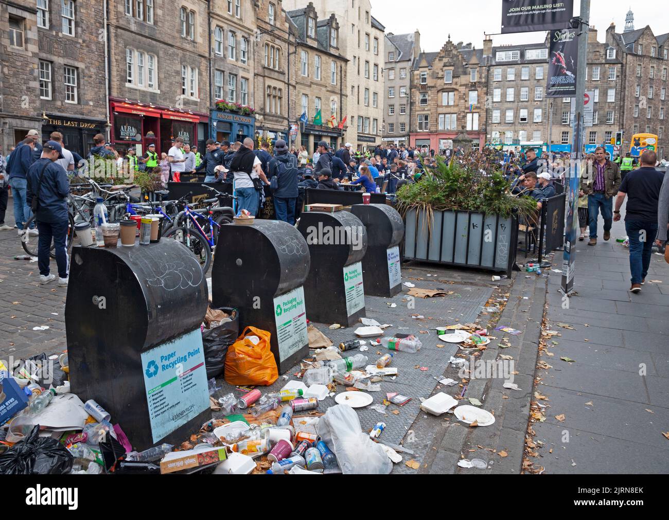 City centre Edinburgh, Scotland, UK. 25th August 2022. Cloudy but mild 19 degrees centigrade for the FC Zurich fans who gathered surrounded by Police Officers in the untidy Grassmarket to peacefully socialise before this evening's game with Heart of Midlothian. Also, smaller crowds in the Royal Mile for street performers. Pictured: Rubbish still piled up at refuse bins due to strike with FC Zurich fans in background having a drink in the Grassmarket. Credit: ArchWhite/alamy live news. Stock Photo
