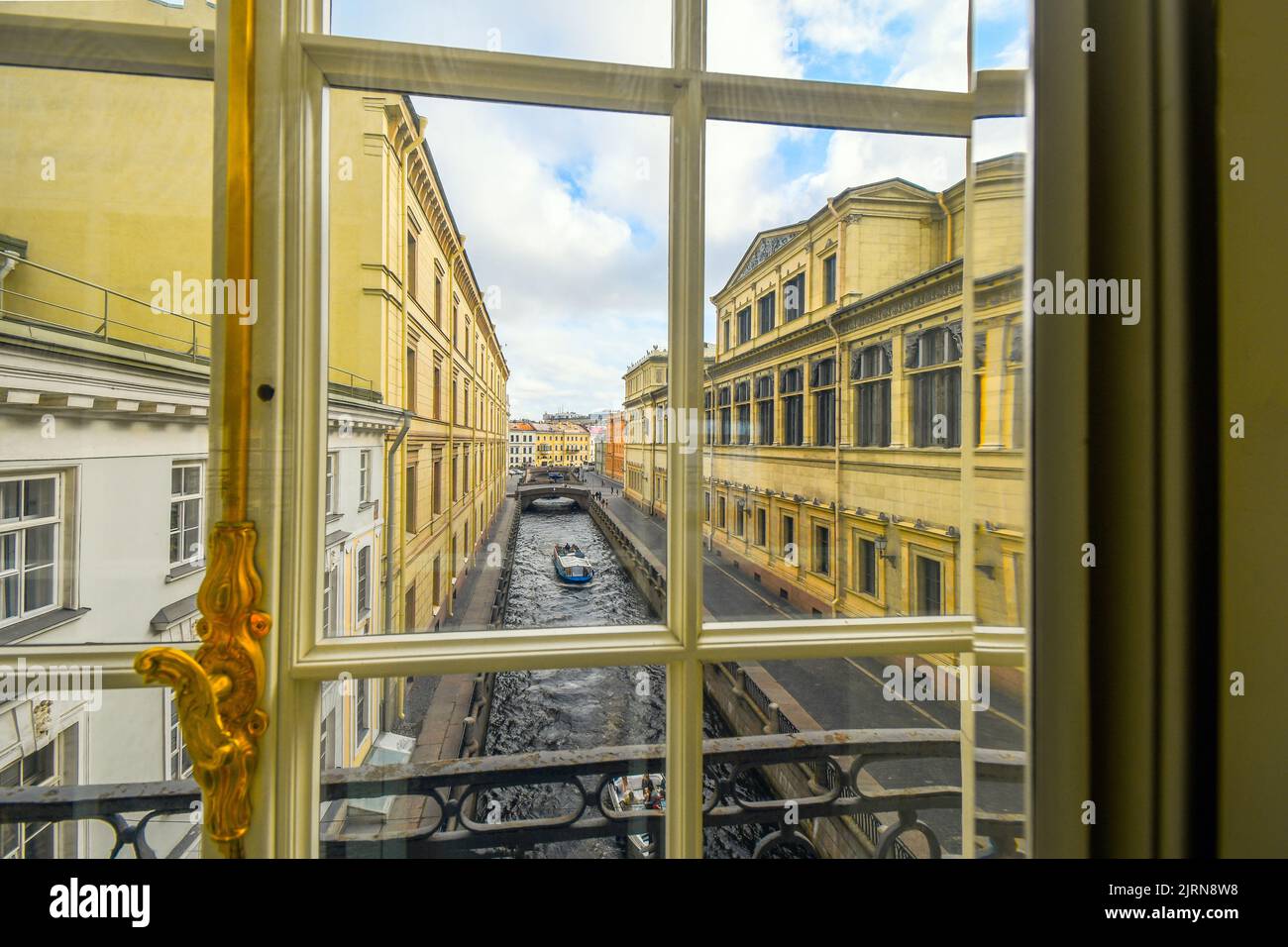 A tour boat glides down the Zimnyaya Kanavka Winter Canal and the Neva River in St. Petersburg Russia, view from a gallery window inside the Hermitage Stock Photo