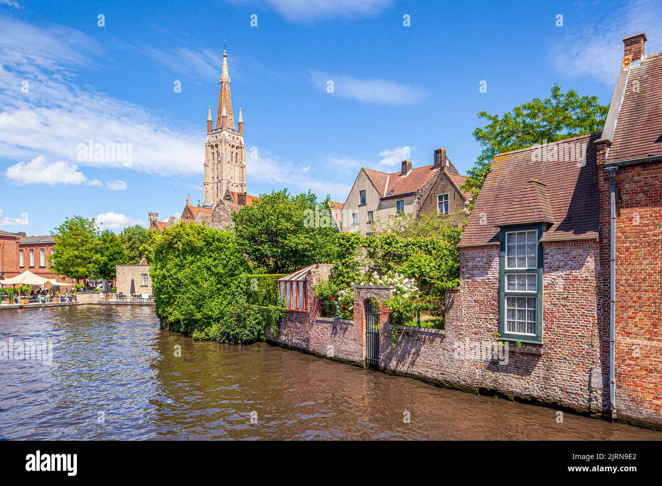 The spire of the Church of Our Lady (Onze-Lieve-Vrouwekerk) overlooking old houses beside the canal in Bruges, Belgium Stock Photo