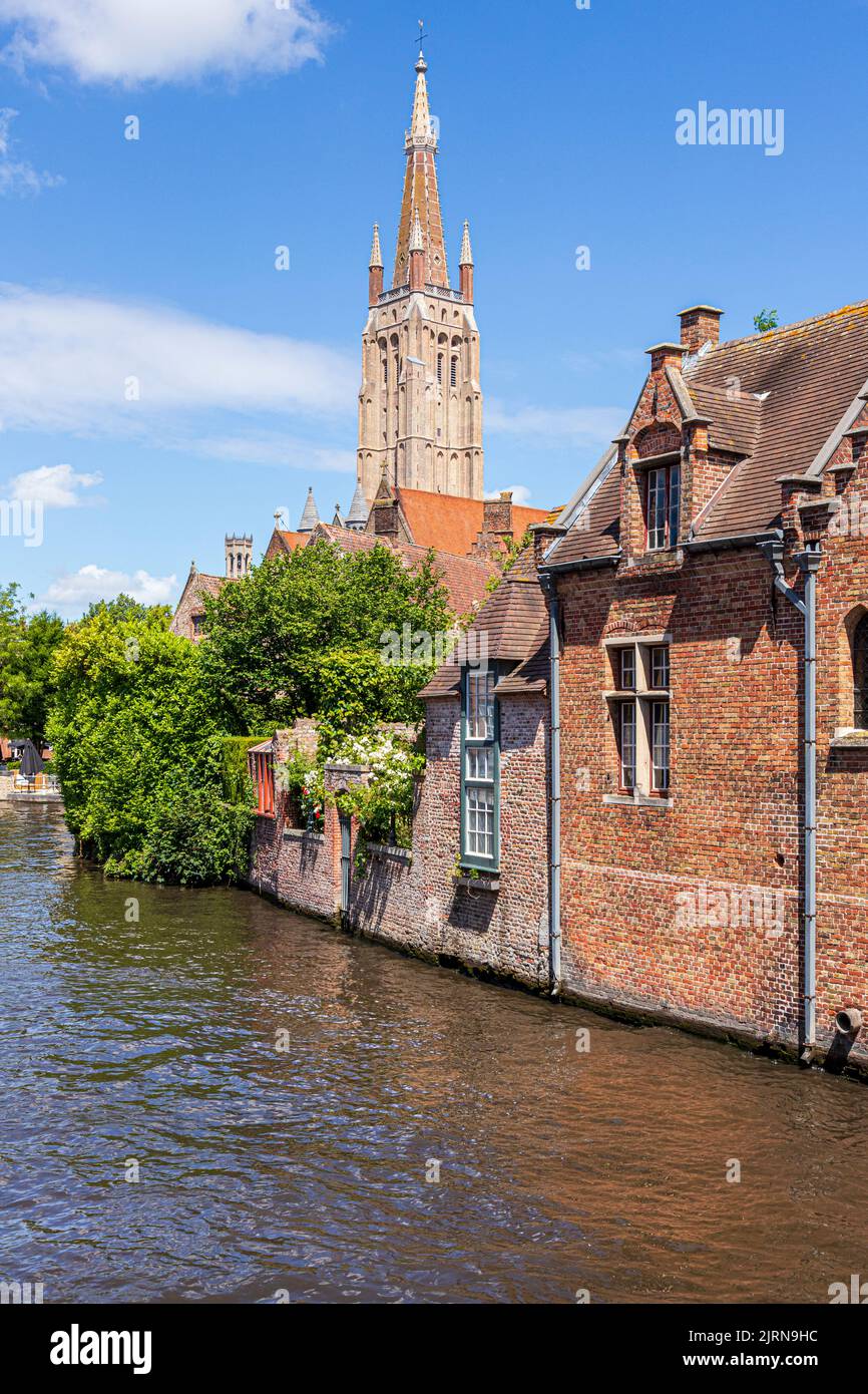 The spire of the Church of Our Lady (Onze-Lieve-Vrouwekerk) overlooking old houses the canal in Bruges, Belgium Stock Photo