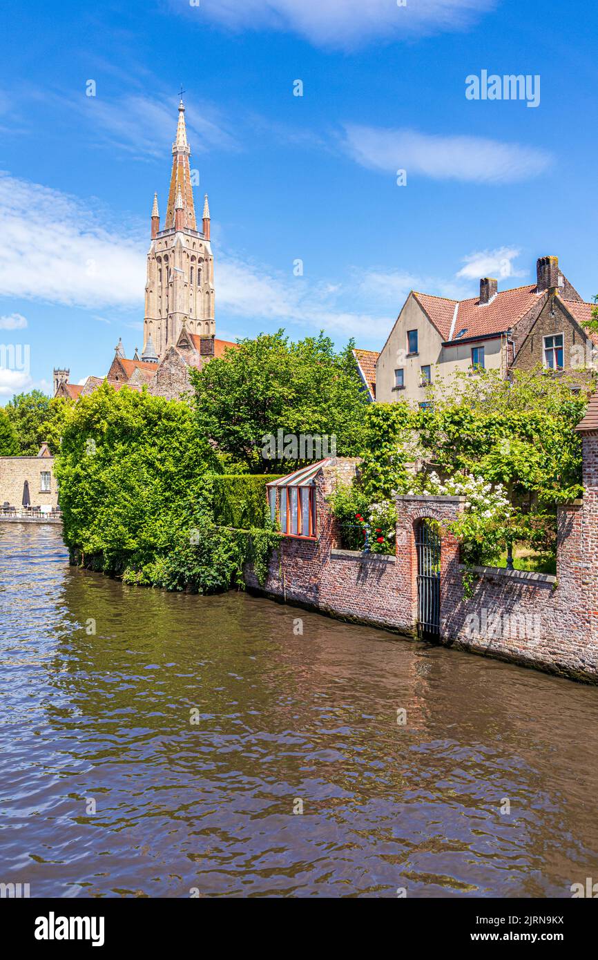 The spire of the Church of Our Lady (Onze-Lieve-Vrouwekerk) overlooking old houses beside the canal in Bruges, Belgium Stock Photo