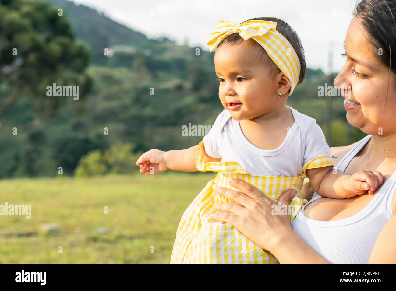 latin mother holding her daughter in an outdoor field, smiling and living a beautiful family moment. summer day with mom. concept of joy. Stock Photo