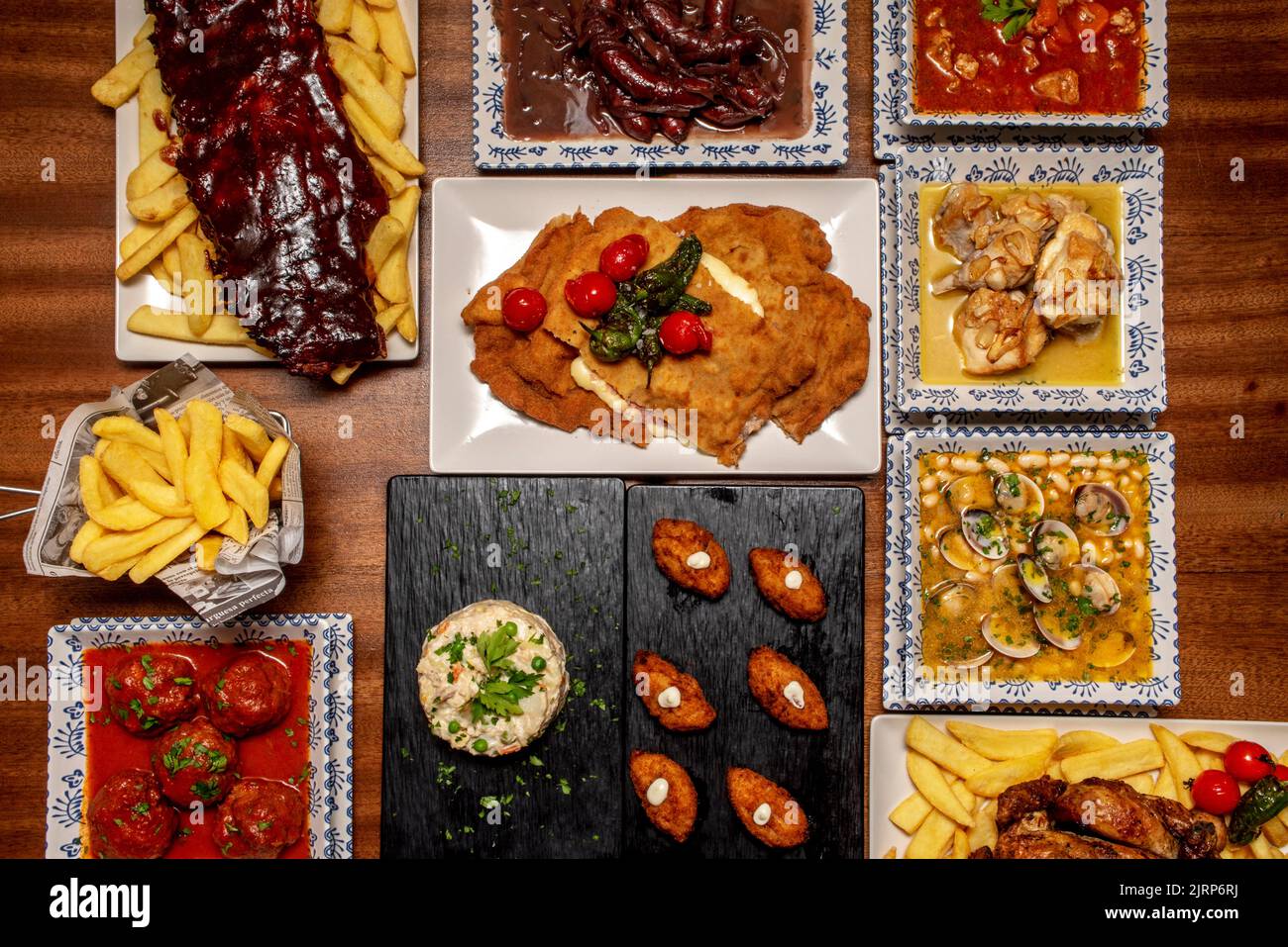 Plates and trays of typical recipes of Spanish gastronomy with croquette tapas, meatballs, beans with clams, garlic chicken, wine sausages and Russian Stock Photo